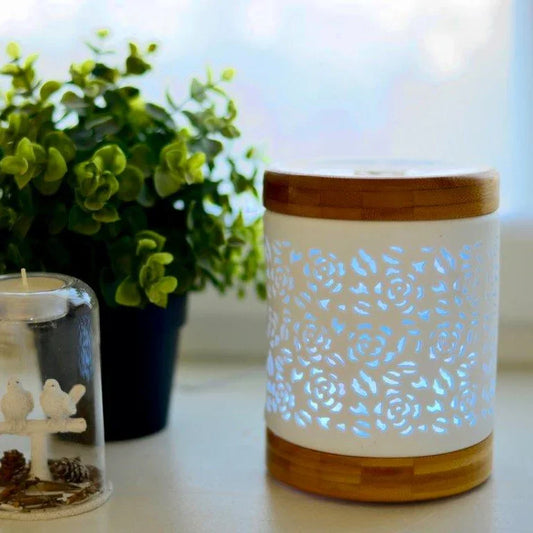 Keramische cilindervormige diffuser met bamboe deksel en witte bloemenpatroon, naast kaars en groen plantje