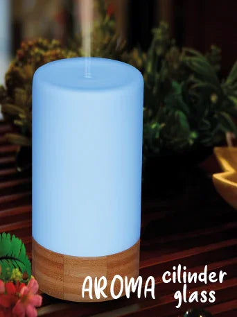 Witte aroma diffuser cilinder van glas met houten basis op houten tafel, omlijst door planten