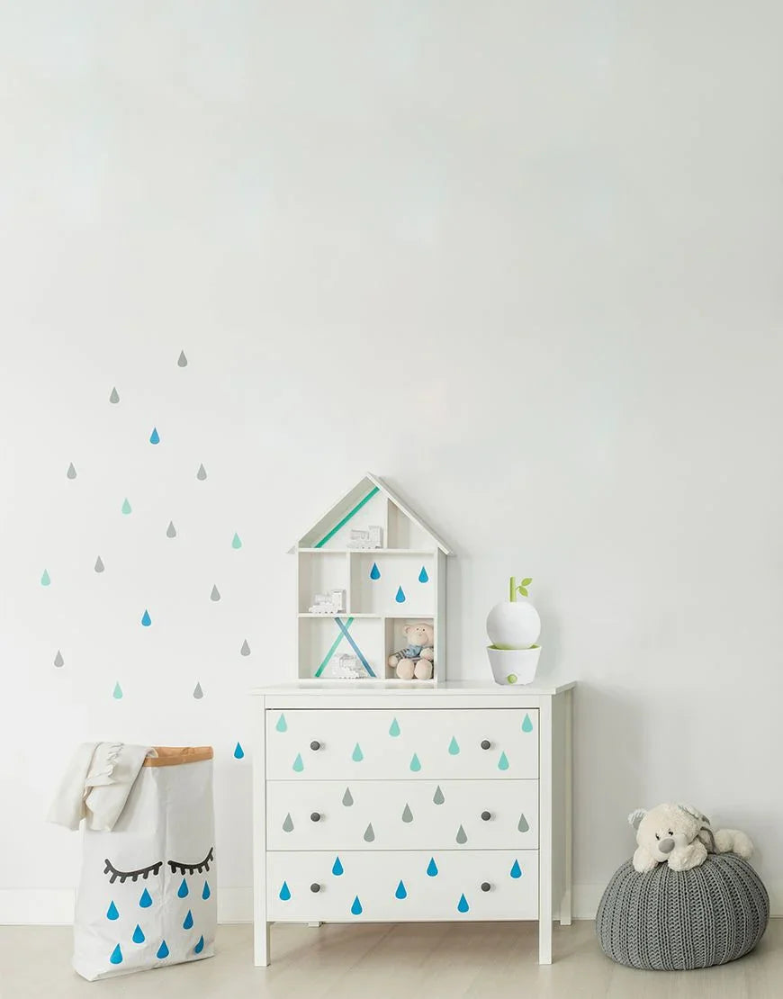 Minimalistische babykamer met witte ladekast met blauwe en grijze druppelstickers, speelgoed en knuffels