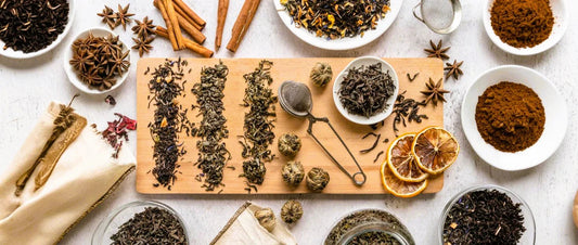 Houten snijplank met verschillende droge theesoorten, steranijs, kaneelstokjes en gedroogde citroen op witte ondergrond