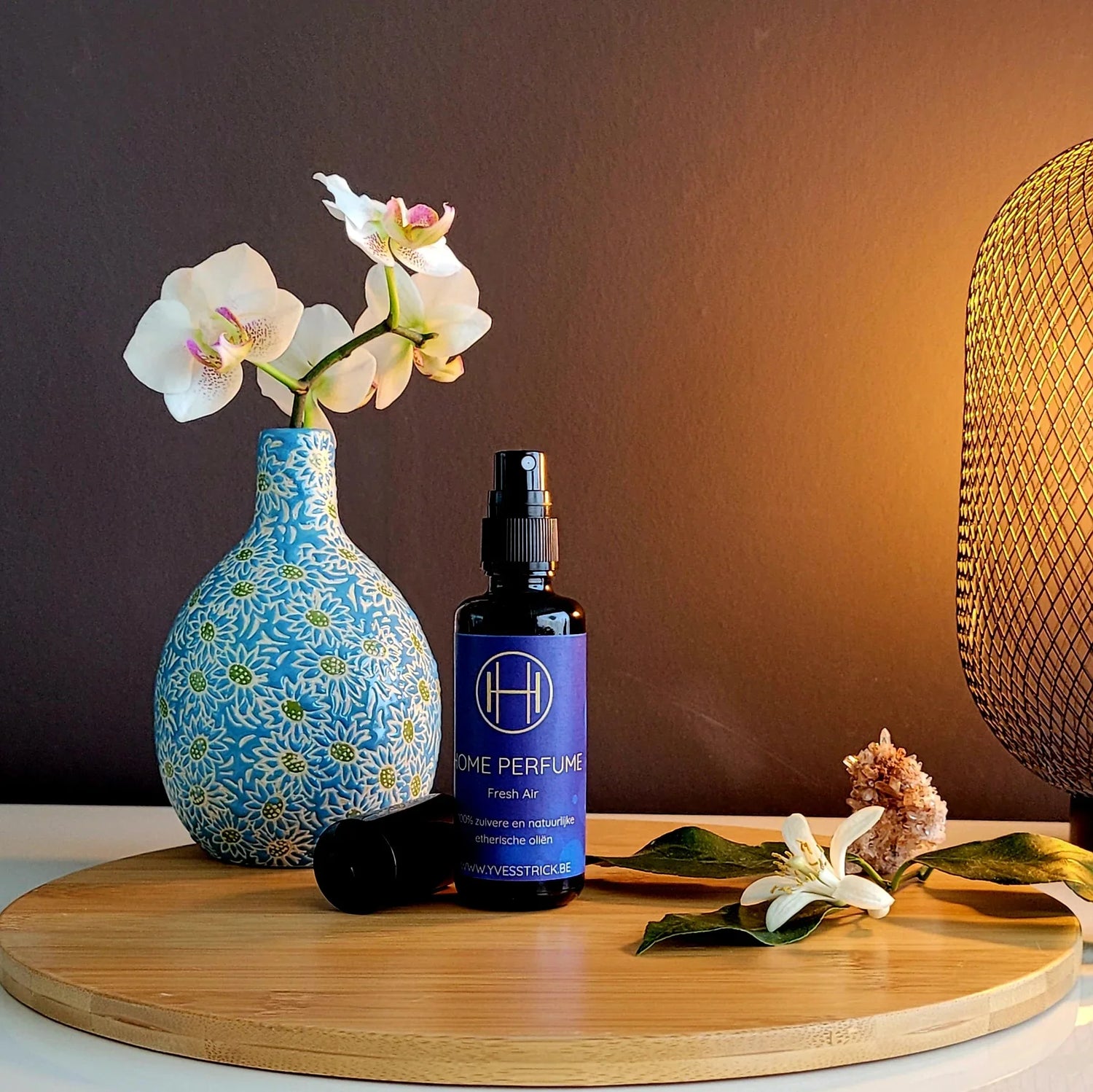 Blauwe vaas met witte orchidee, flesje Home Perfume Fresh Air spray, sfeervolle lamp op houten plateau