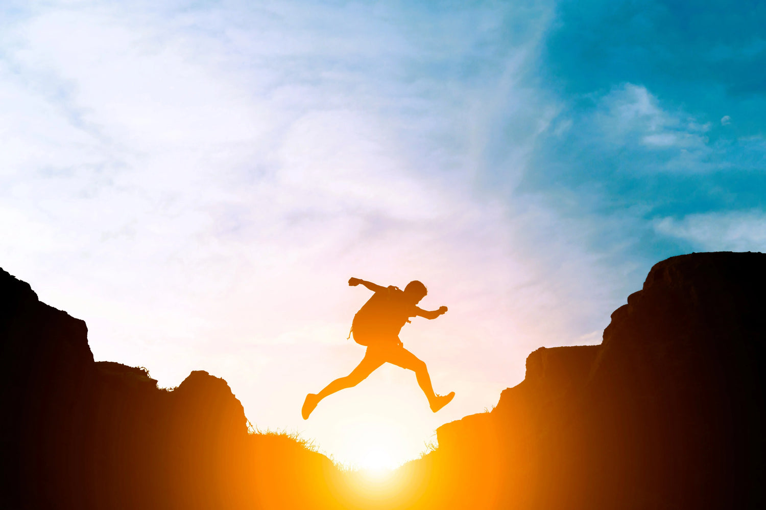 Silhouet van man met rugzak springend tussen rotsen op zonsondergang in buitenlandschap
